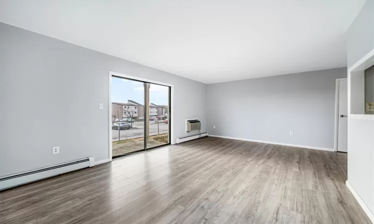 Unfurnished living room featuring a wall mounted AC, light hardwood / wood-style flooring, and baseboard heating