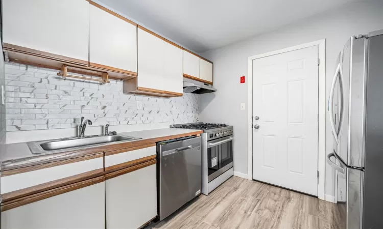 Kitchen featuring light wood-type flooring, backsplash, stainless steel appliances, sink, and white cabinets