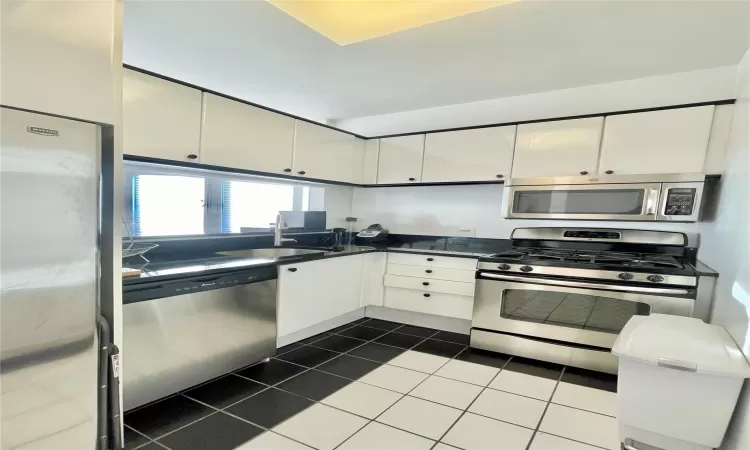 Kitchen featuring white cabinetry, sink, dark tile patterned floors, and appliances with stainless steel finishes