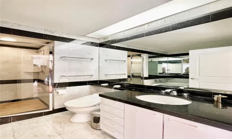 Bathroom with vanity, toilet, a tile shower, and tile walls