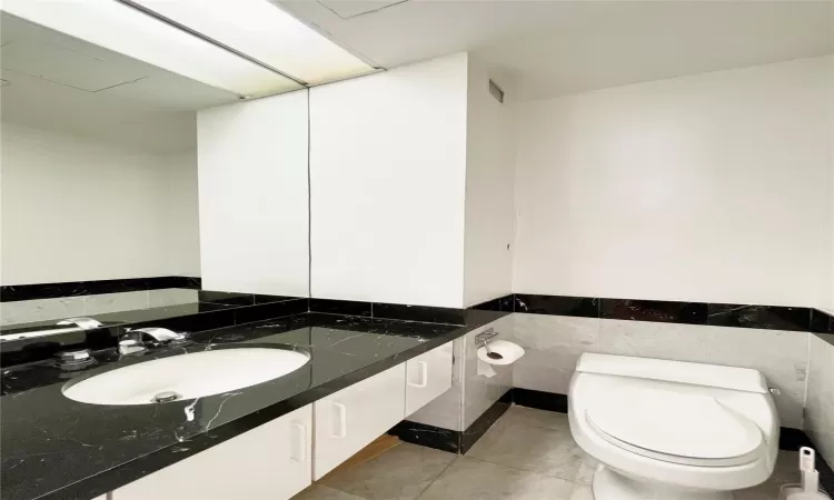 Bathroom featuring tile patterned flooring, vanity, toilet, and tile walls