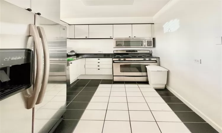 Kitchen featuring tile patterned flooring, appliances with stainless steel finishes, and white cabinetry