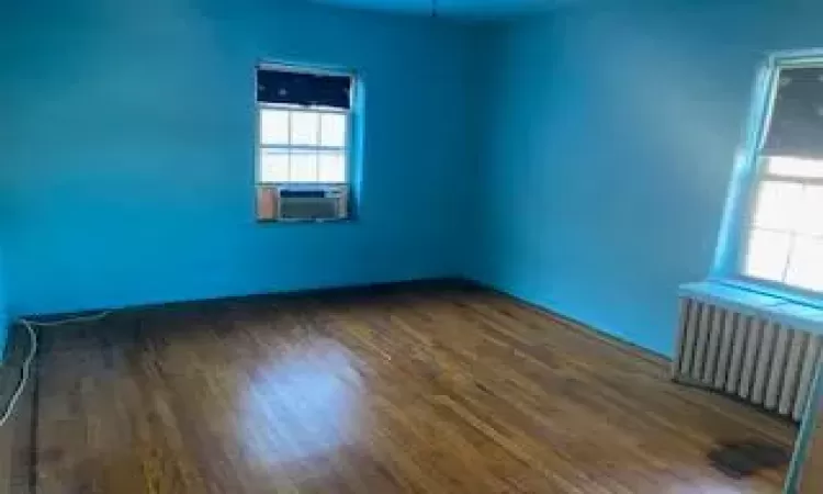 Empty room featuring plenty of natural light, cooling unit, dark hardwood / wood-style flooring, and radiator