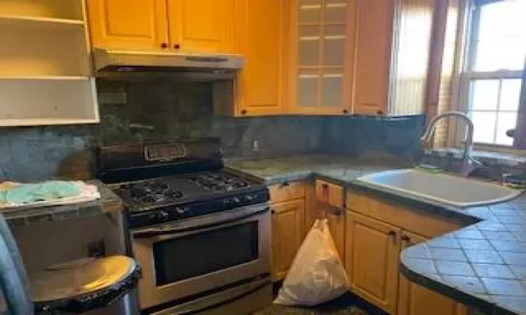 Kitchen featuring stainless steel stove, tile counters, tasteful backsplash, and sink