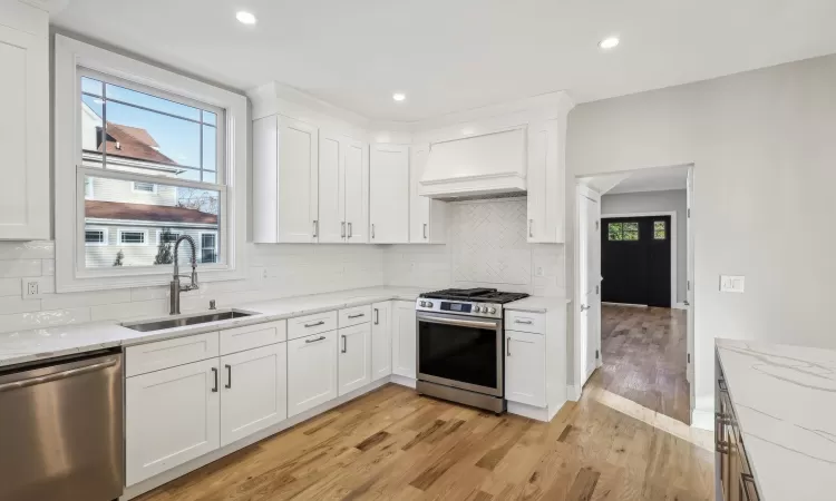 Kitchen featuring white cabinetry, sink, stainless steel appliances, backsplash, and custom exhaust hood