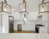 Kitchen featuring white cabinets, sink, light stone countertops, appliances with stainless steel finishes, and decorative light fixtures