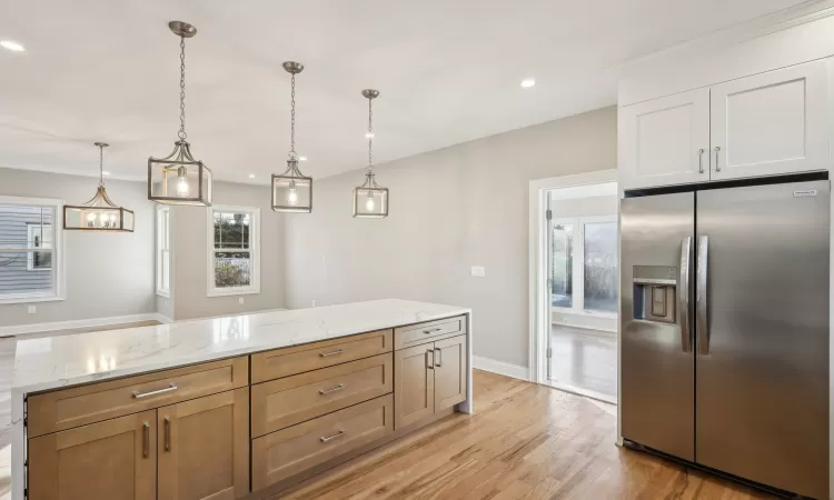 Kitchen featuring pendant lighting, white cabinets, stainless steel fridge, light hardwood / wood-style floors, and light stone counters