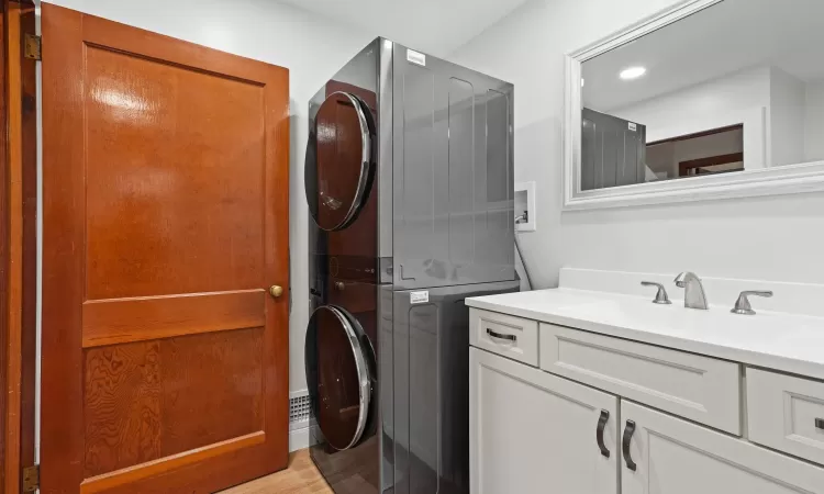 Washroom featuring stacked washer / dryer, sink, cabinets, and light hardwood / wood-style flooring