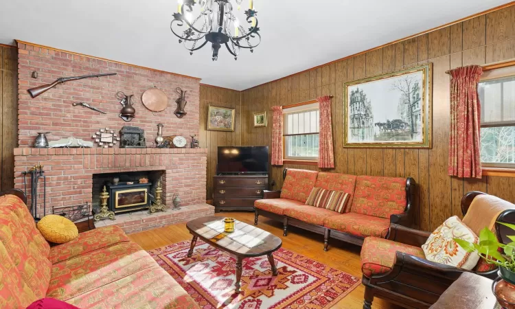 Living room with hardwood / wood-style floors, a wood stove, a notable chandelier, and wood walls