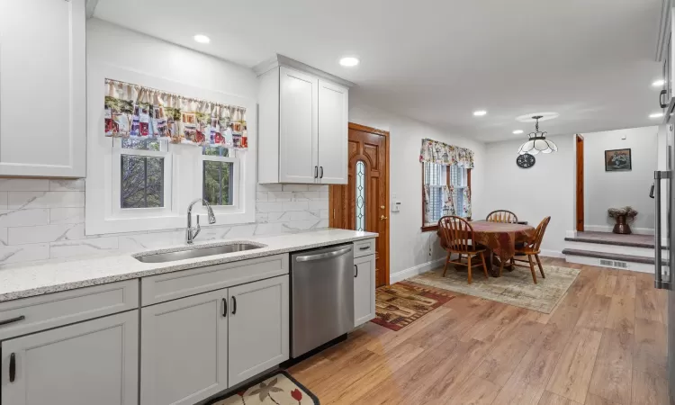 Kitchen featuring tasteful backsplash, light stone countertops, dishwasher, and sink