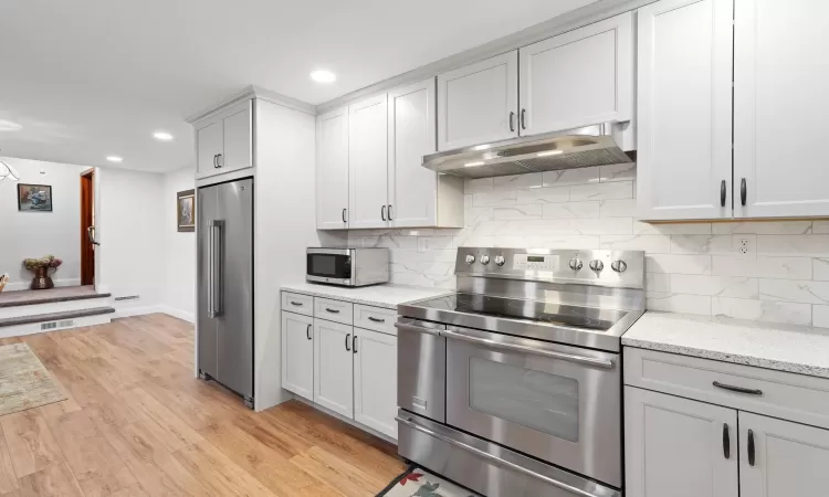 Kitchen with decorative backsplash, light stone countertops, light hardwood / wood-style flooring, and appliances with stainless steel finishes