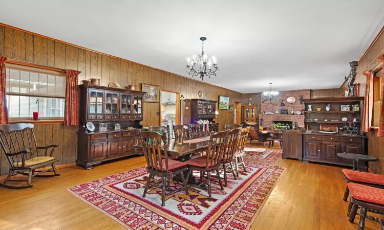 Dining space featuring a fireplace, wooden walls, light hardwood / wood-style floors, and a notable chandelier