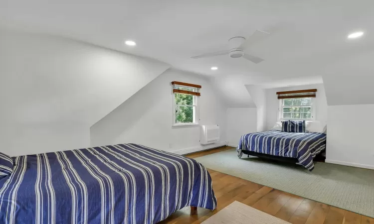 Bedroom with vaulted ceiling, ceiling fan, baseboard heating, wood-type flooring, and a wall unit AC