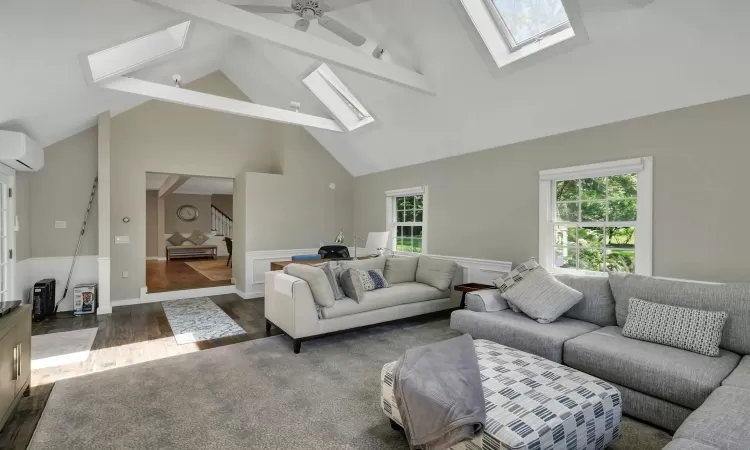 Living room featuring ceiling fan, a healthy amount of sunlight, an AC wall unit, and lofted ceiling with skylight