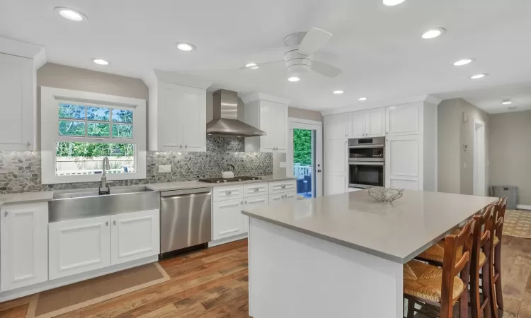 Kitchen with a center island, sink, stainless steel appliances, wall chimney range hood, and white cabinets