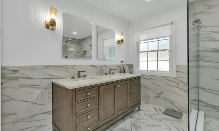 Bathroom with a tile shower, vanity, and tile walls