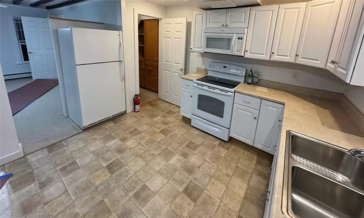 Kitchen with white cabinets, white appliances, baseboard heating, and sink