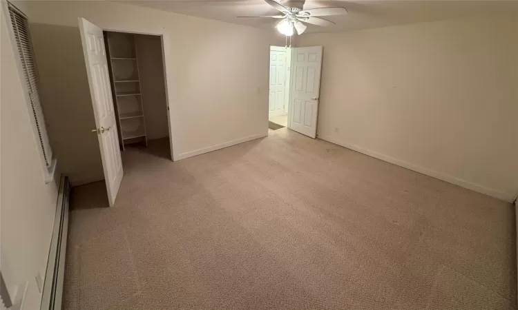 Unfurnished bedroom featuring light carpet, a closet, ceiling fan, and a baseboard heating unit