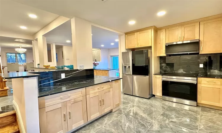 Kitchen featuring kitchen peninsula, appliances with stainless steel finishes, light brown cabinets, and a notable chandelier