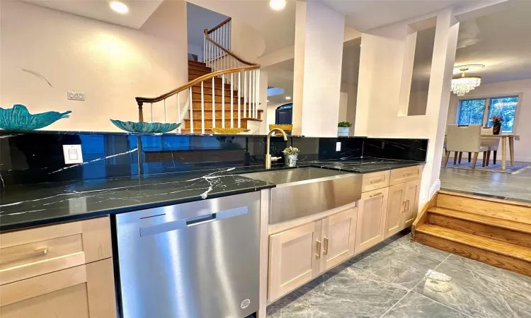 Kitchen with dishwasher, light brown cabinets, dark stone counters, sink, and a notable chandelier