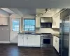 Kitchen with wall chimney range hood, white cabinetry, high end appliances, and sink