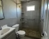 Bathroom featuring vanity, toilet, a shower with shower door, and tile walls, Stone flooring in shower.