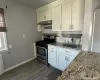 Kitchen featuring light stone countertops, tasteful backsplash, sink, white cabinets, and stainless steel stove