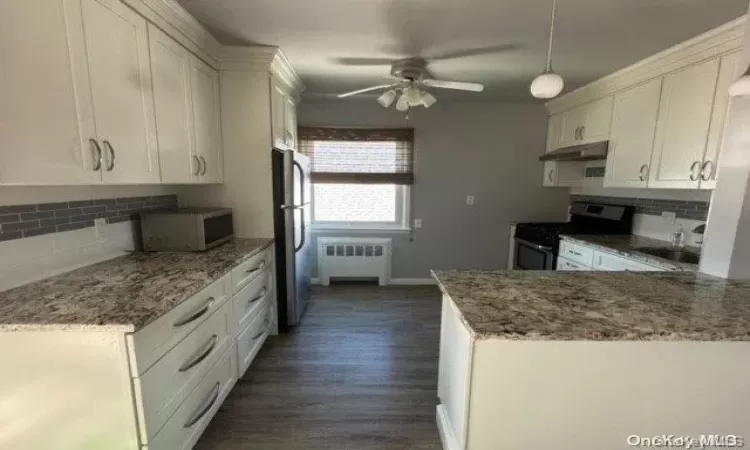 Kitchen with stone counters, hanging light fixtures, stainless steel appliances, and decorative backsplash