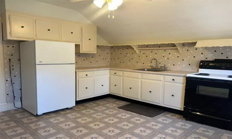 Kitchen featuring sink, black electric range oven, white refrigerator, lofted ceiling, and white cabinets