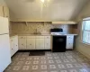 Kitchen with white refrigerator, sink, vaulted ceiling, black electric range, and white cabinetry