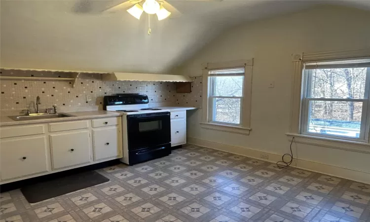 Kitchen featuring decorative backsplash, vaulted ceiling, sink, white cabinets, and black electric range oven