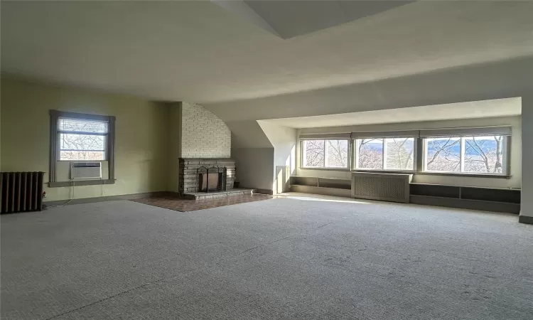 Unfurnished living room featuring carpet, lofted ceiling, radiator heating unit, and a fireplace