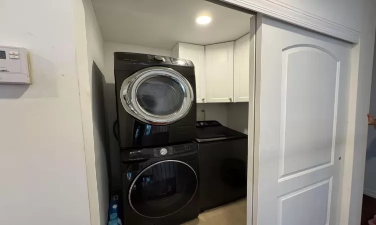 Washroom featuring cabinets, stacked washer / dryer, and light tile patterned flooring