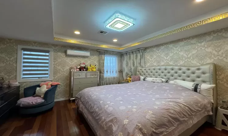 Bedroom featuring dark hardwood / wood-style floors, a wall unit AC, and a tray ceiling