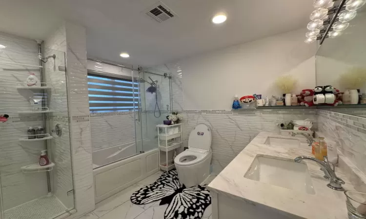 Full bathroom featuring vanity, toilet, bath / shower combo with glass door, and tile walls