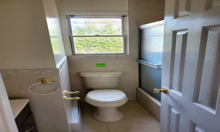 Full bathroom with vanity, tile patterned floors, toilet, enclosed tub / shower combo, and tile walls