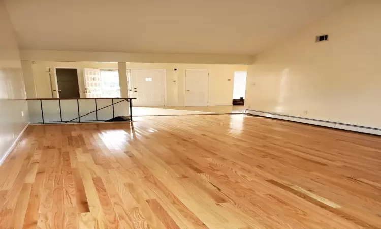 Unfurnished room featuring vaulted ceiling, a baseboard heating unit, and light wood-type flooring