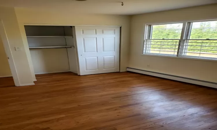 Unfurnished bedroom with dark hardwood / wood-style floors, a closet, and a baseboard radiator