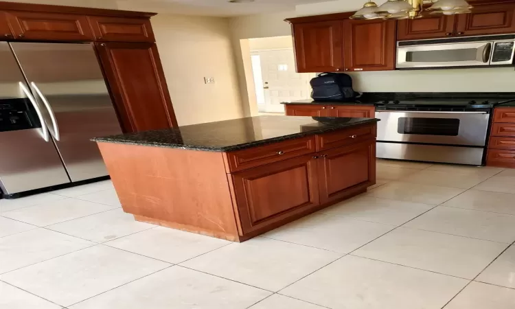 Kitchen featuring appliances with stainless steel finishes, an inviting chandelier, dark stone countertops, a center island, and light tile patterned flooring