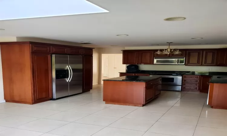 Kitchen featuring stainless steel appliances, light tile patterned floors, an inviting chandelier, a center island, and hanging light fixtures