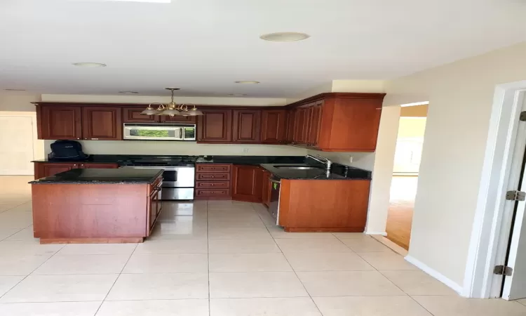 Kitchen featuring sink, a kitchen island, light tile patterned flooring, stainless steel appliances, and a chandelier