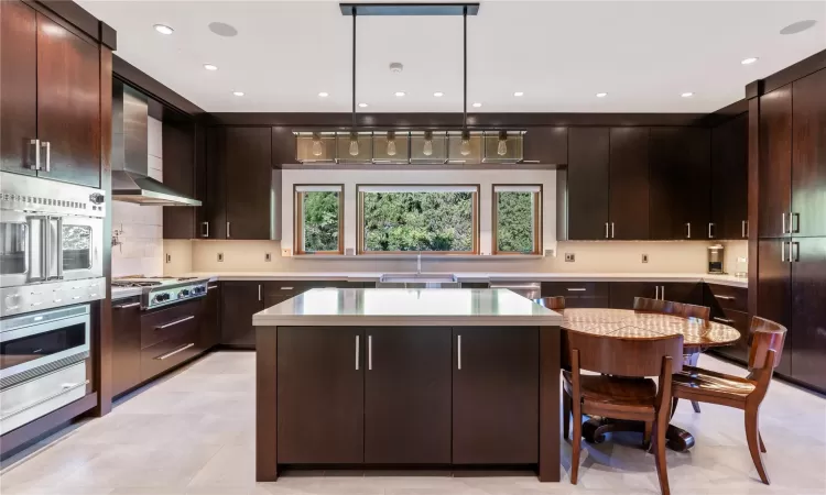 Kitchen featuring a center island, sink, wall chimney range hood, decorative light fixtures, and dark brown cabinets