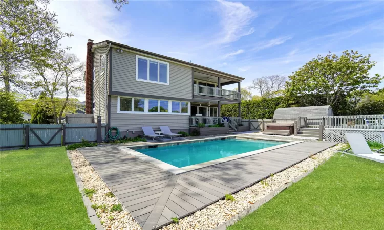 Rear view of property featuring a yard, a swimming pool with hot tub, and a balcony