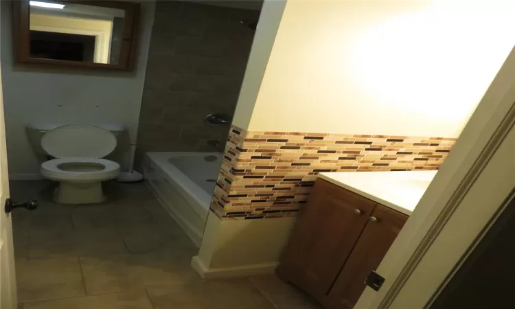 Full bathroom with tile patterned floors, vanity, tiled shower / bath combo, and toilet