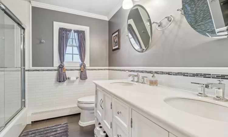 Bathroom with toilet, vanity, tile walls, and a baseboard heating unit