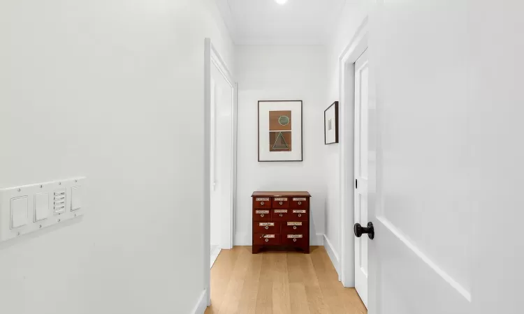 Hallway with light wood-type flooring and ornamental molding