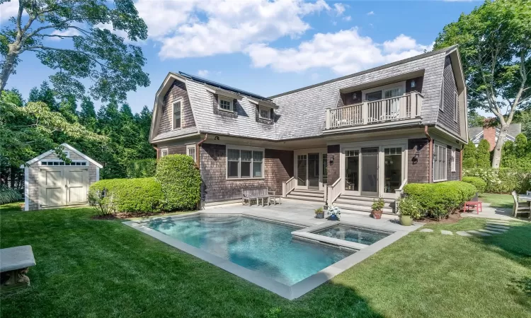 Rear view of property with a swimming pool with hot tub, a balcony, a yard, a shed, and a patio area