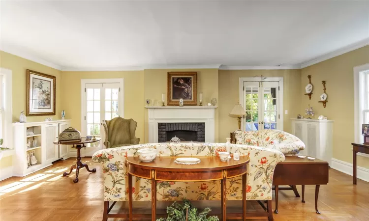 Living room with french doors, light parquet flooring, ornamental molding, and a brick fireplace