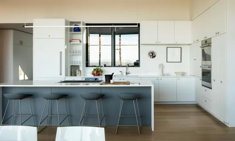 Kitchen with white cabinetry, double oven, a breakfast bar area, and sink