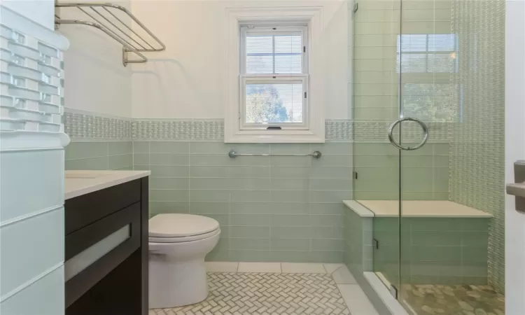 Bathroom with vanity, tile patterned floors, toilet, tile walls, and a shower with shower door